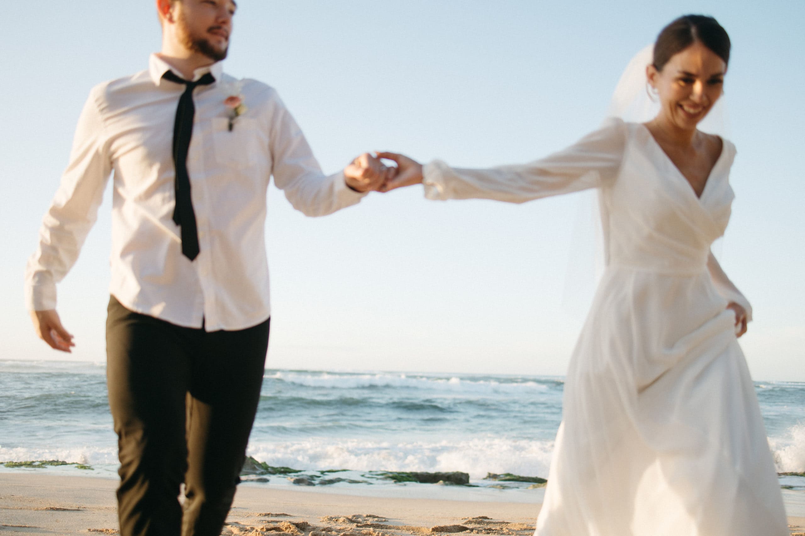 bride and groom are holding hands and running on the beach