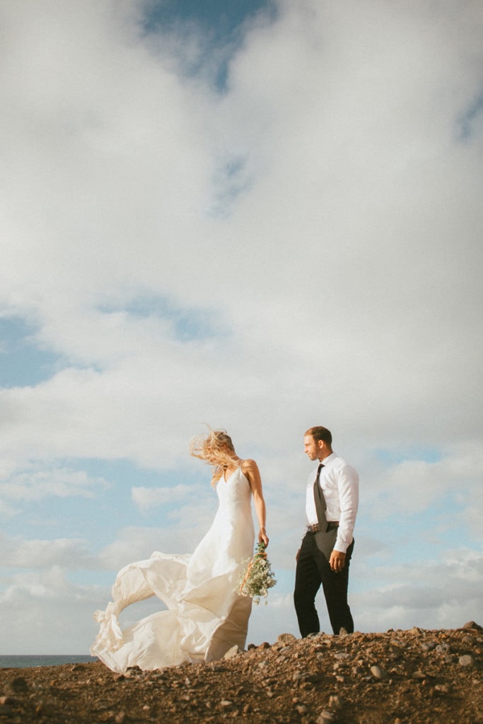 Oahu Elopement Photographer, bride and groom walking along rock wall, wind blowing her dress
