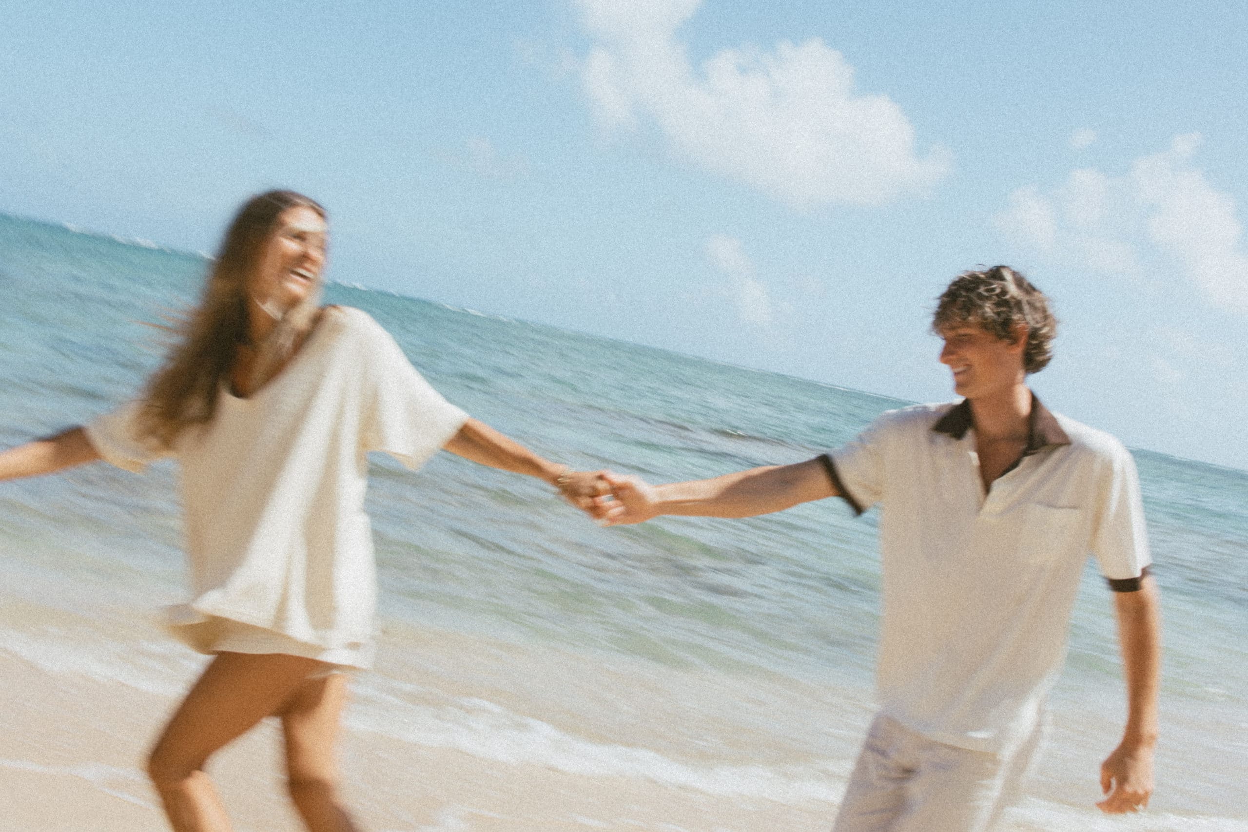couple is holding hands, running on the beach while laughing