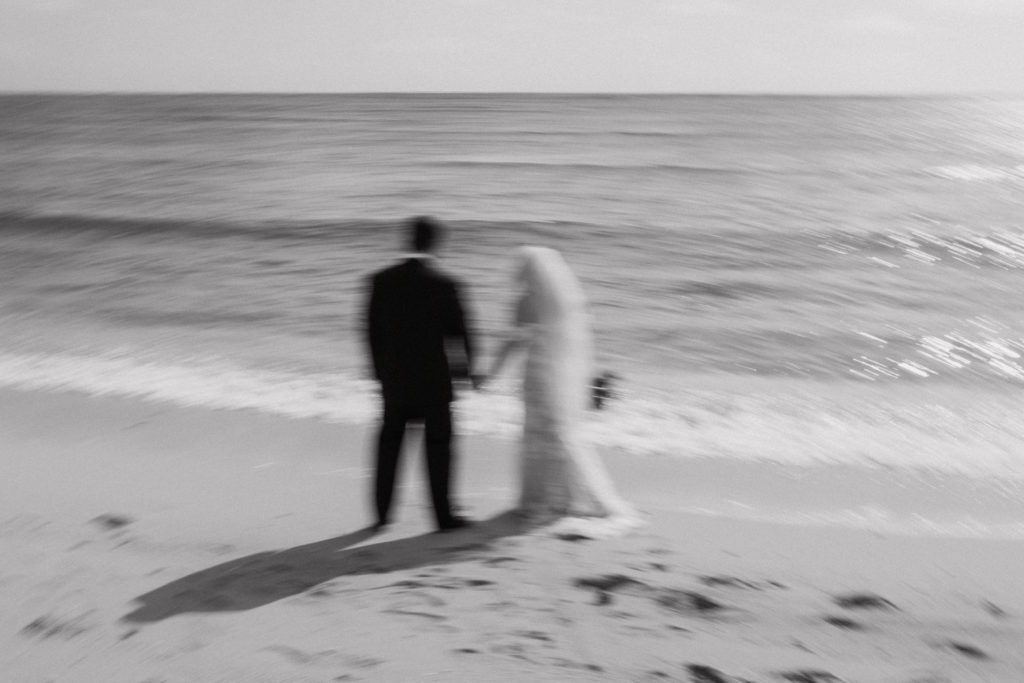 black and white blurry picture of the bride and groom holding hands on the beach