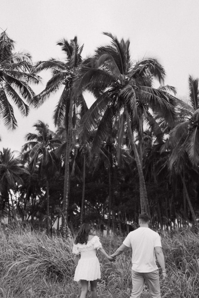 black and white portrait of couple holding hands walking into tropical forest