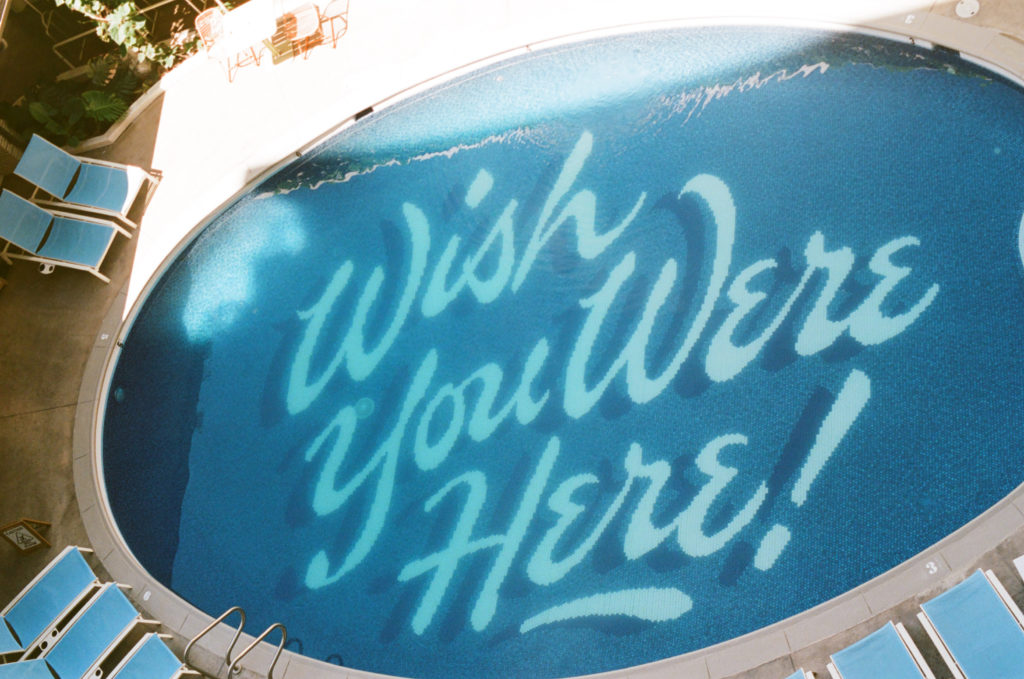 Film picture of the Surf Jacks Hotel pool that has the writing "wish you were here!"