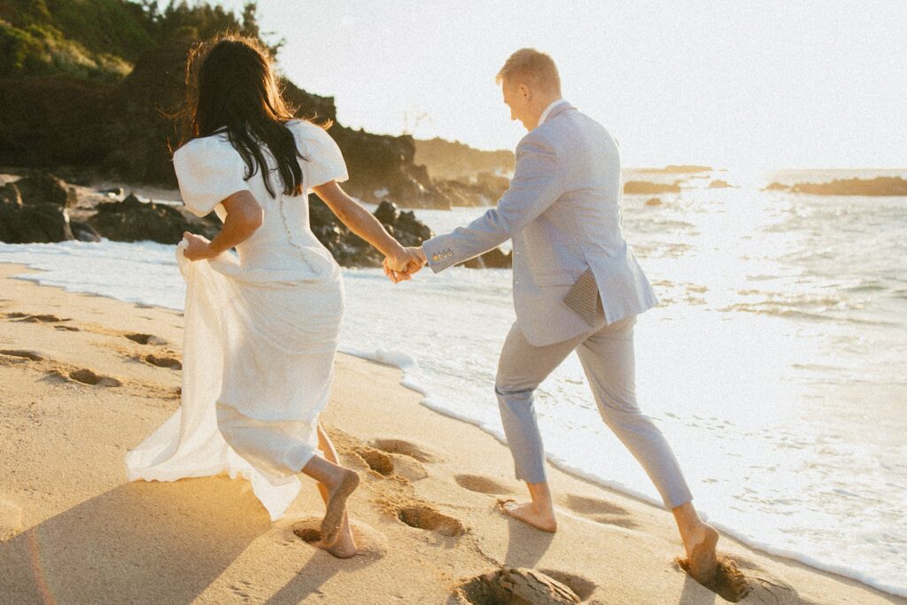 shot of the couple running along the beach while holding hands during golden hour