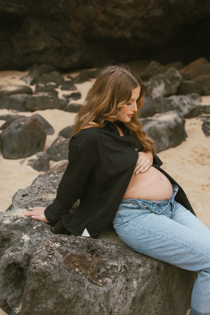 expecting mother is sitting on a rock while holding pregnant stomach and looking down