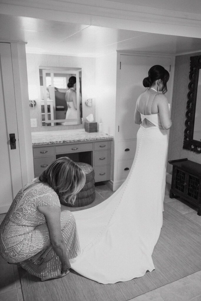 black and white shot of the mother of the bride fixing her dresses train