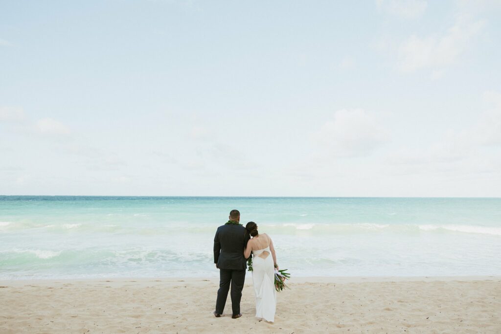 shot of the bride adn groom hugging while looking at the ocean