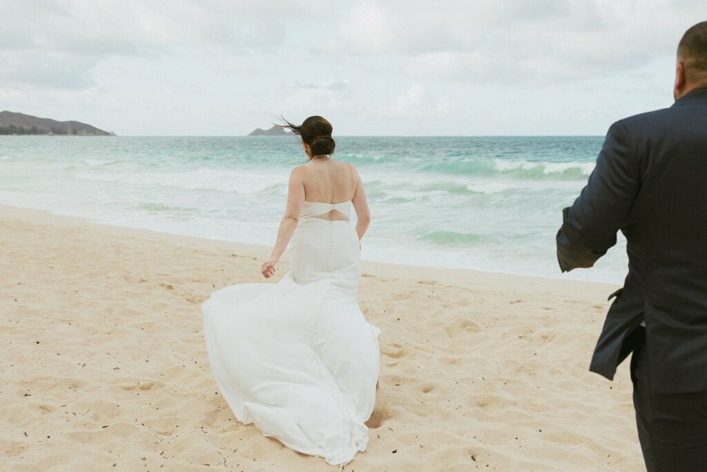 bride walking in front of groom on the beach