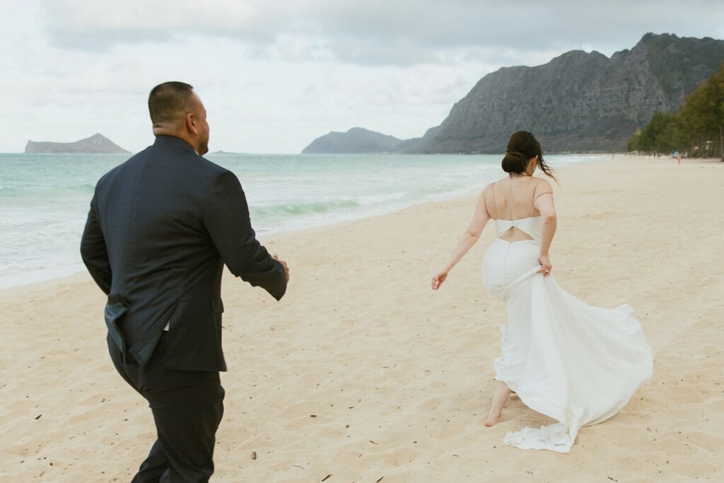 shot of groom walking behind the bride as they walk along the shoreline