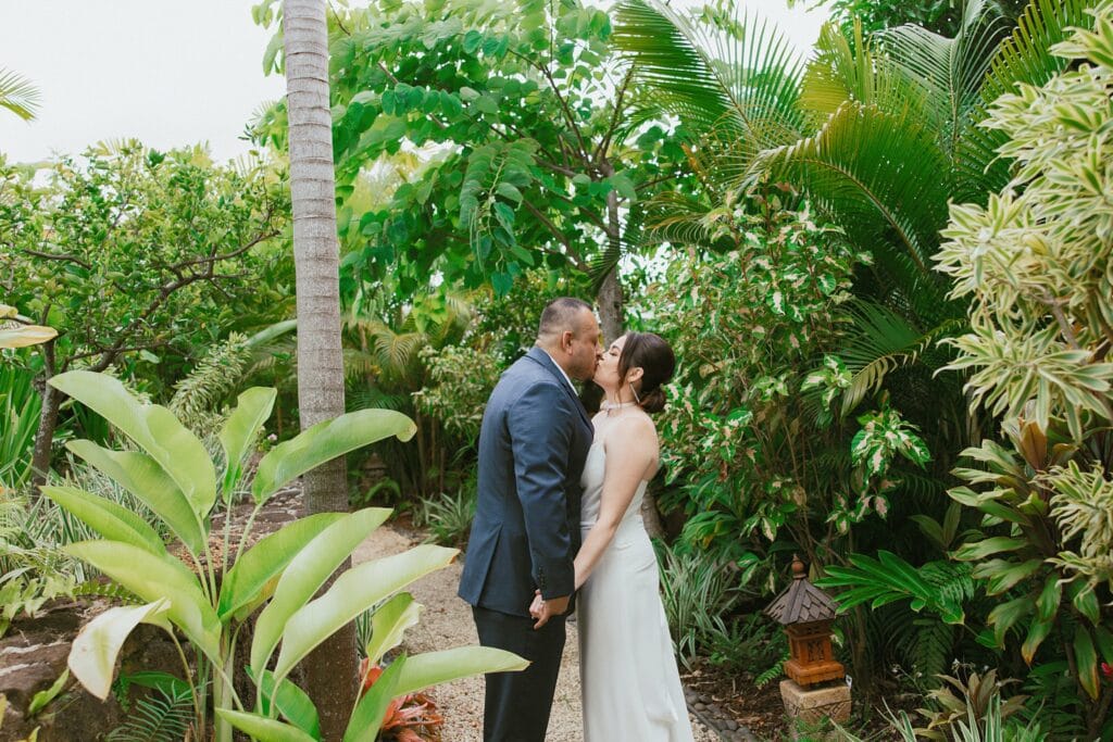 bride and groom are kissing and are standing in tropical green forestry