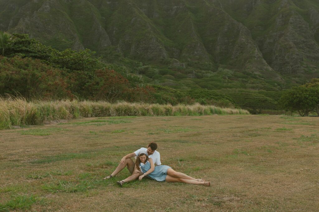 couple is laying down in front of the mountains and picking at the grass together