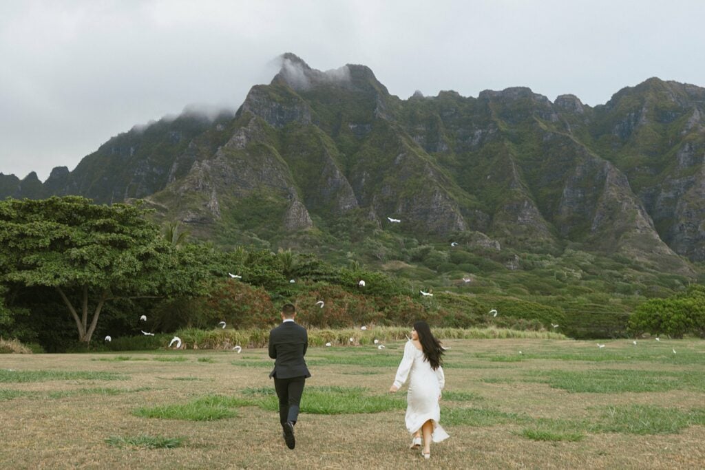 couple is running towards the mountains while white birds fly away
