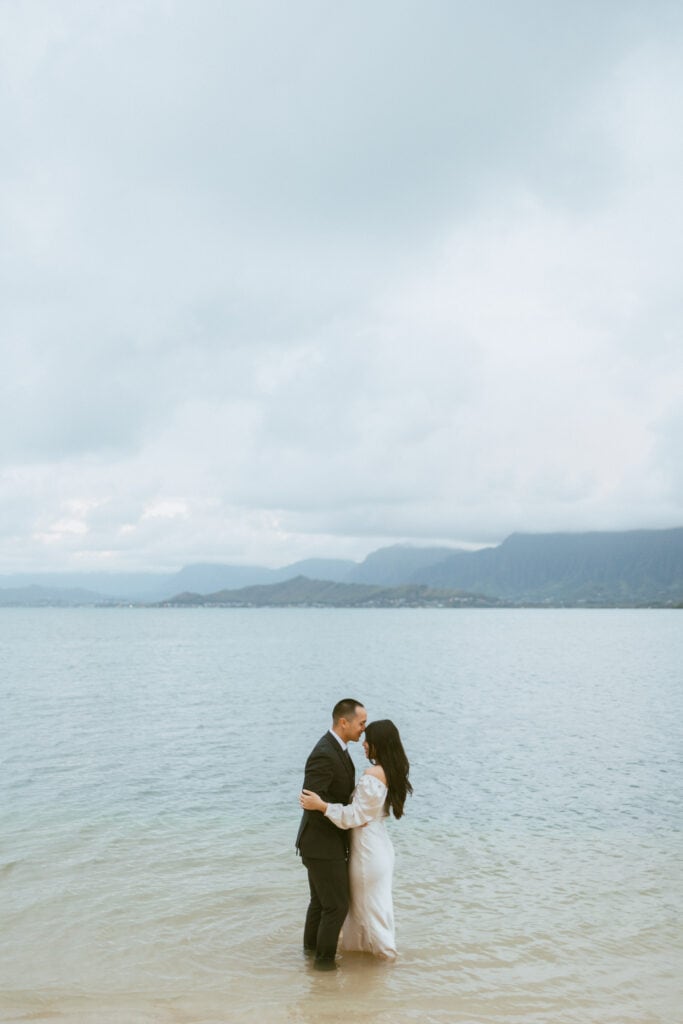 couple is standing in the ocean and hugging as hao kisses julies forehead