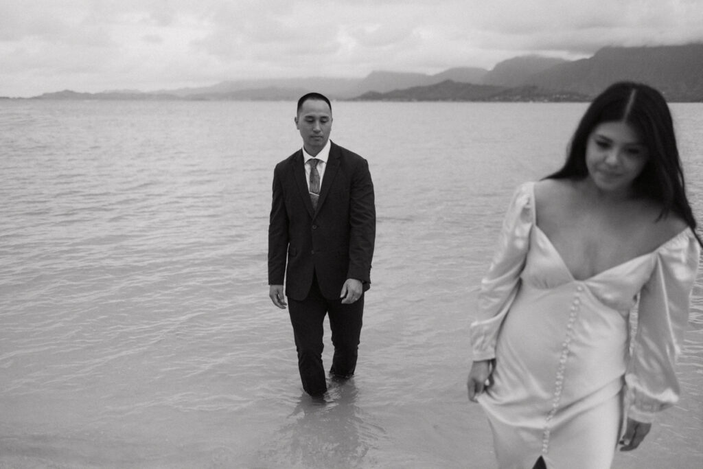 black and white photo of hao and julie walking to the shoreline from the ocean