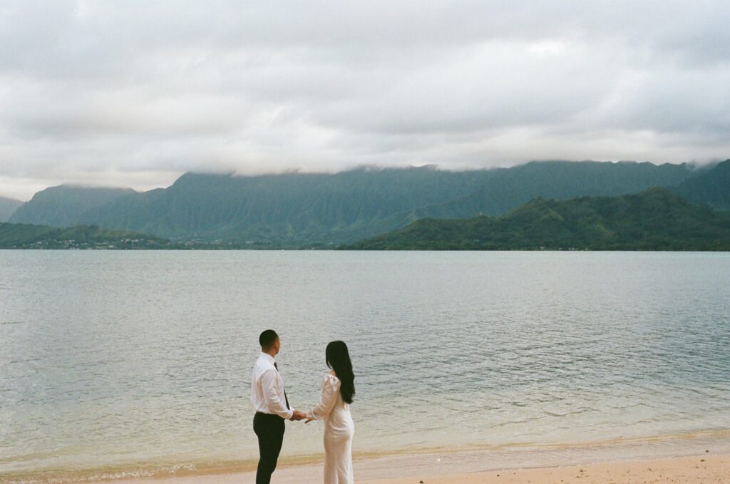film photo of the couple holding hands along the beaches shore and looking off into the ocean