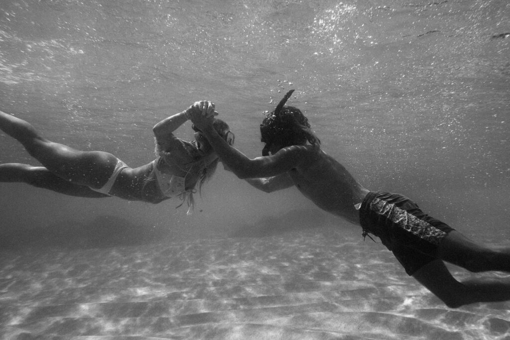 underwater black and white photo of the couple holding hands underwater