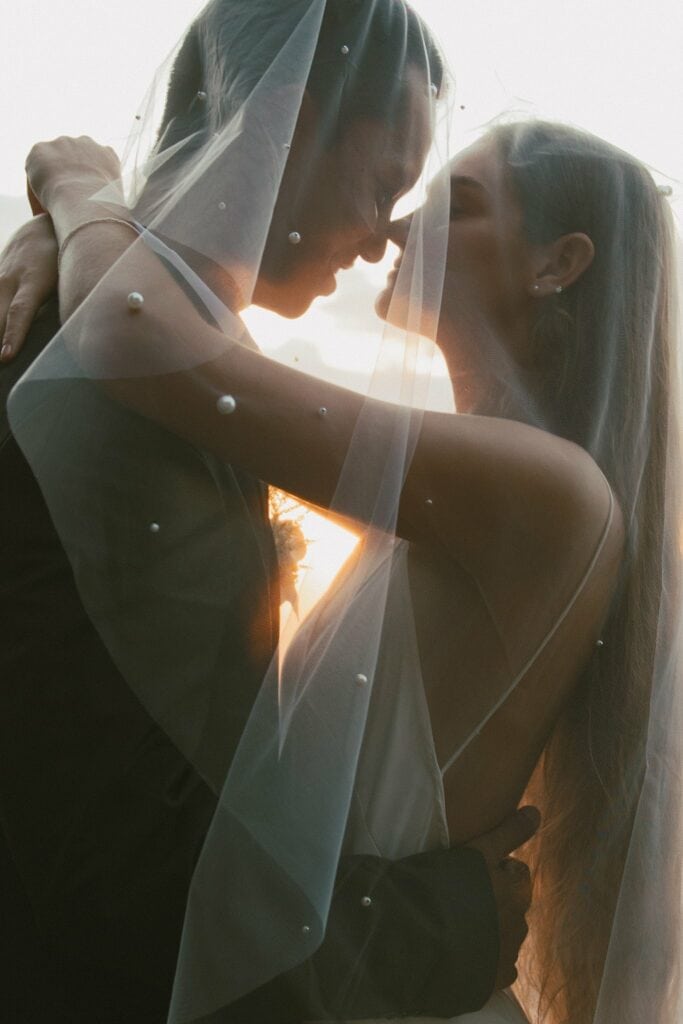 portrait shot of the bride and groom kissing under the veil