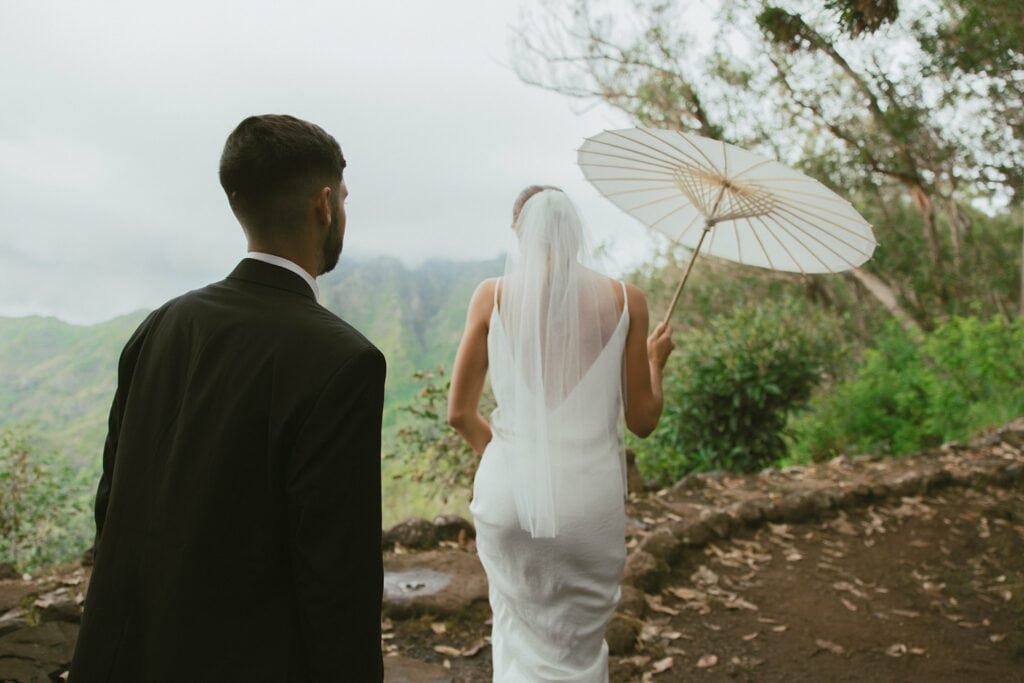 bride and groom are walking while bride holds an umbrella