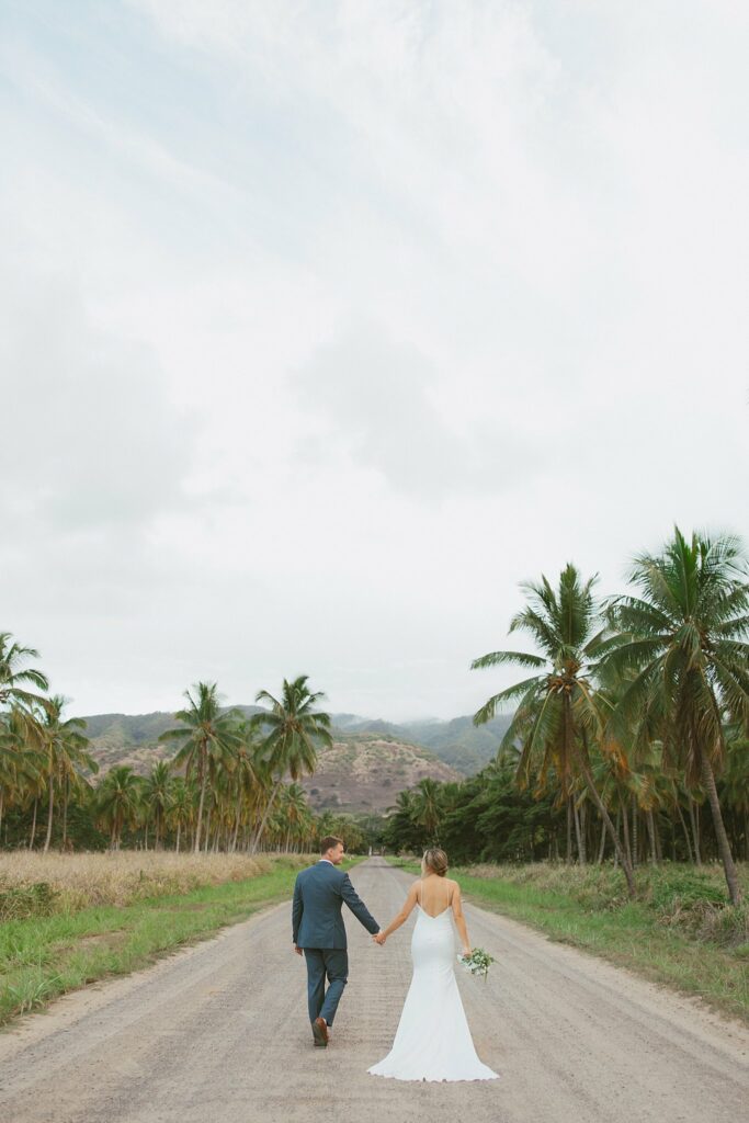 bride and groom are holding hands walking down a dirt road