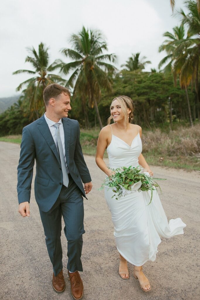 bride and groom are smiling at each other while walking down the dirt road at their destination wedding