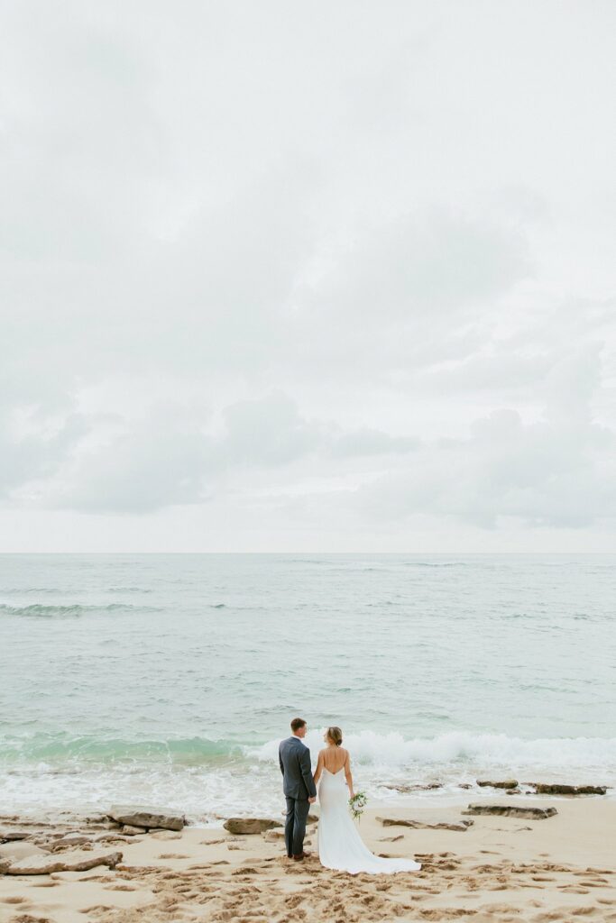bride and groom are looking at the ocean with each other