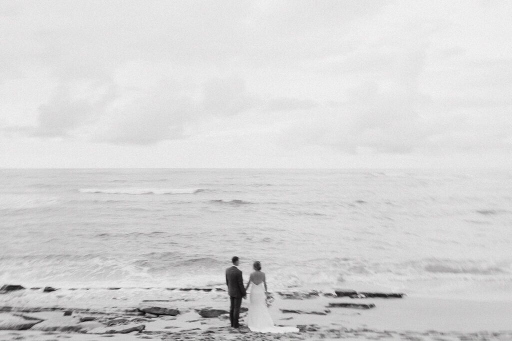 black and white shot of bride and groom looking at the ocean