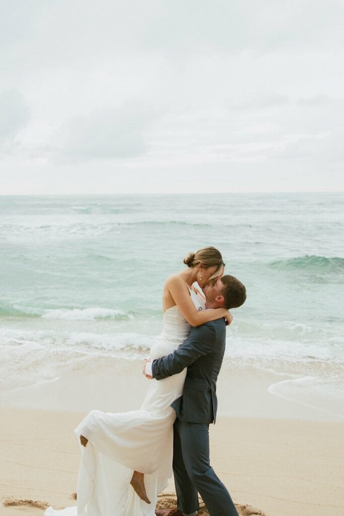bride and groom are kissing on the beach
