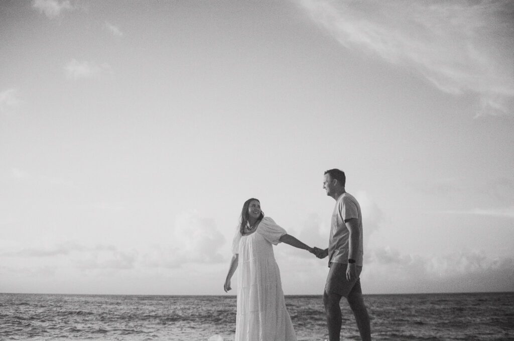 black and white shot of couple holding hands and walking along the beach