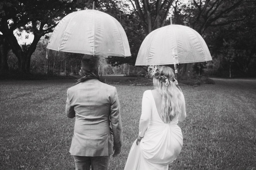 black and white shot of couple holding umbrellas and walking away from camera