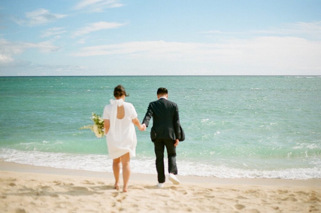 bride and groom are walking towards the ocean