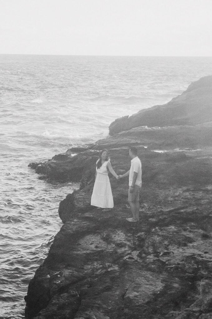shot of couple holding hands while standing on top of a rock