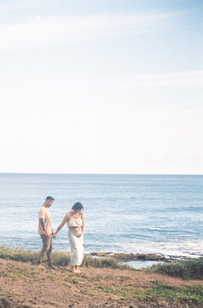 film photo of couple walking along the beach during their oahu beach maternity photoshoot